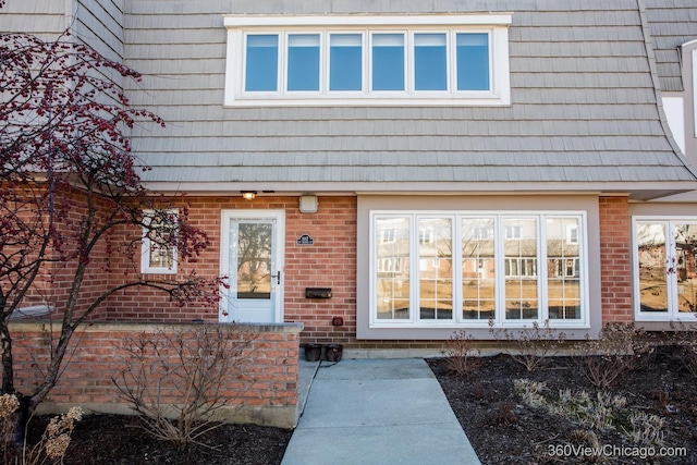 doorway to property featuring brick siding and mansard roof