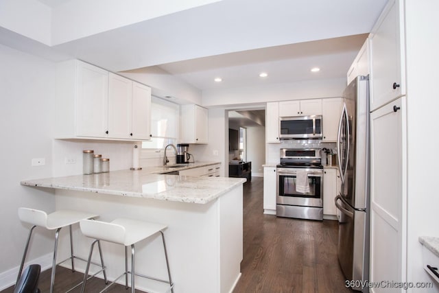 kitchen featuring stainless steel appliances, white cabinets, a peninsula, and light stone counters