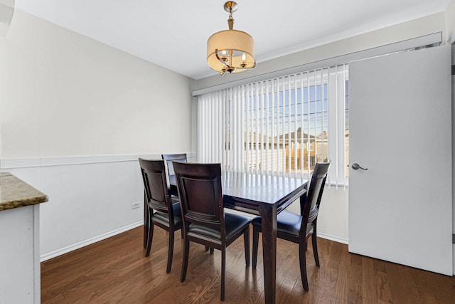 dining space with a wainscoted wall, dark wood finished floors, and an inviting chandelier