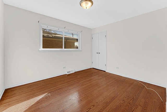 unfurnished room featuring baseboards, visible vents, and wood finished floors