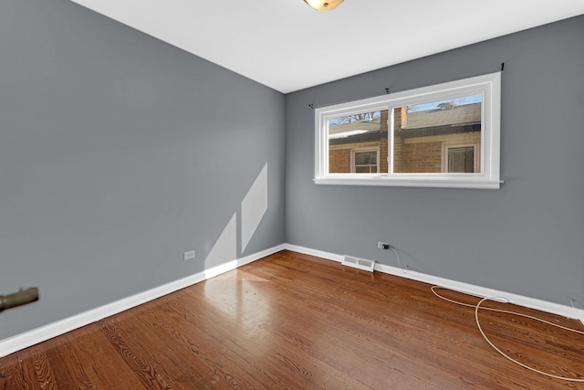 empty room featuring wood finished floors, visible vents, and baseboards