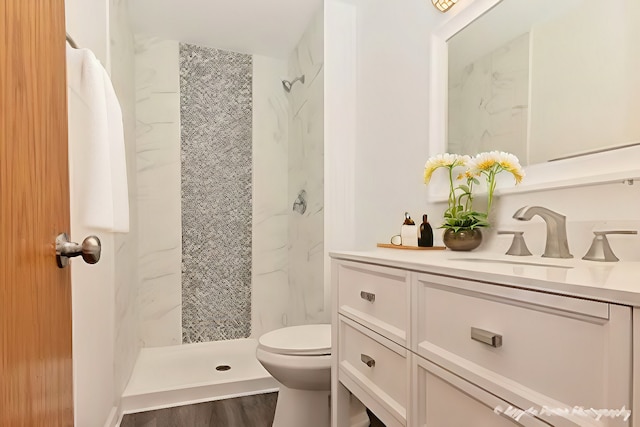 bathroom featuring toilet, wood finished floors, a marble finish shower, and vanity