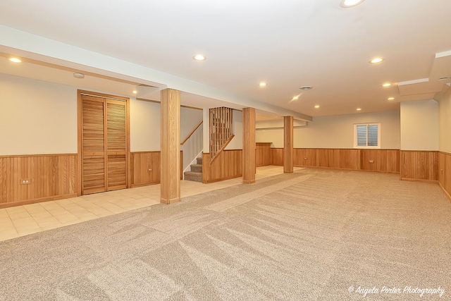 finished below grade area with stairway, light colored carpet, wainscoting, and wooden walls