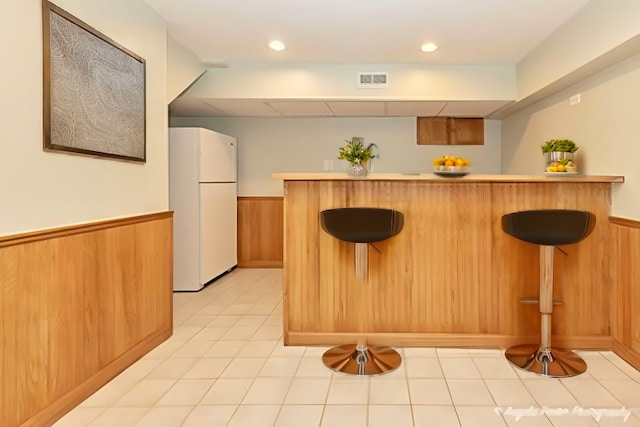 interior space featuring a breakfast bar, freestanding refrigerator, wainscoting, and a peninsula