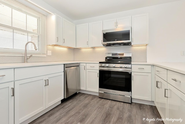 kitchen with light countertops, backsplash, appliances with stainless steel finishes, white cabinetry, and wood finished floors