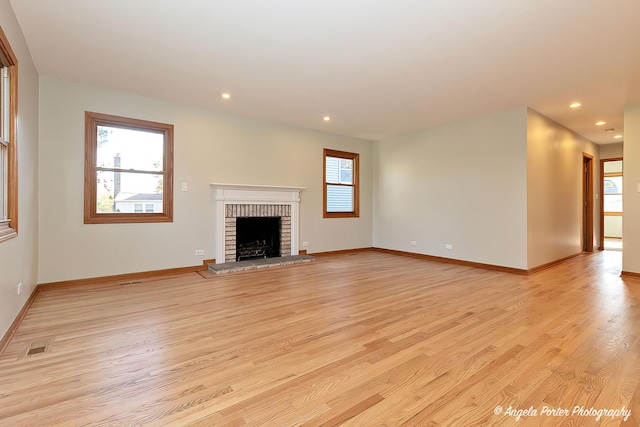 unfurnished living room with a brick fireplace, light wood-style flooring, and a healthy amount of sunlight