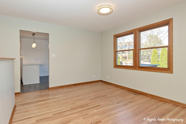 empty room featuring light wood-type flooring, visible vents, and baseboards