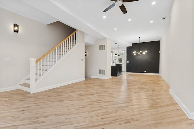 unfurnished living room featuring light wood finished floors, baseboards, visible vents, stairs, and ceiling fan with notable chandelier