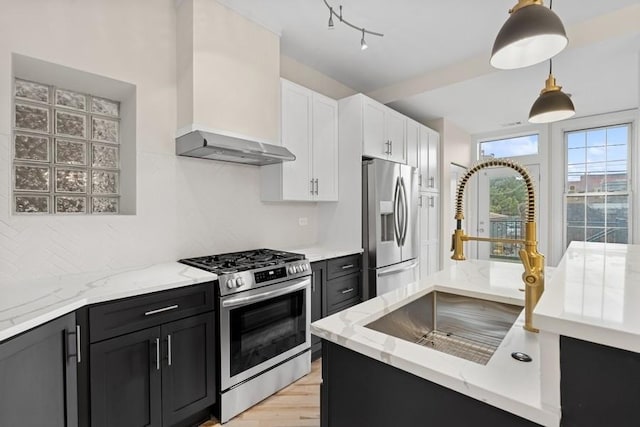 kitchen with hanging light fixtures, appliances with stainless steel finishes, a sink, dark cabinets, and wall chimney exhaust hood