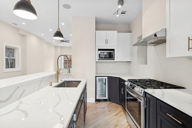 kitchen with stainless steel appliances, white cabinets, a sink, beverage cooler, and wall chimney exhaust hood