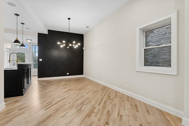 unfurnished dining area featuring light wood finished floors, an inviting chandelier, an accent wall, a sink, and baseboards