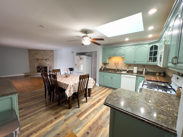 kitchen featuring a skylight, backsplash, a sink, white appliances, and green cabinetry