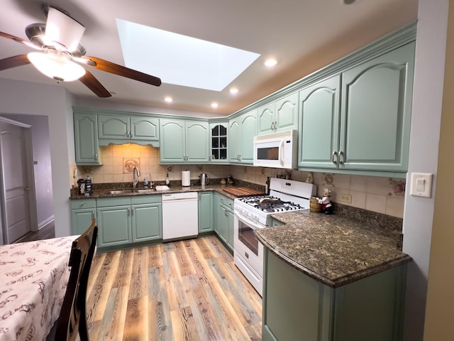 kitchen featuring a skylight, green cabinets, glass insert cabinets, a sink, and white appliances