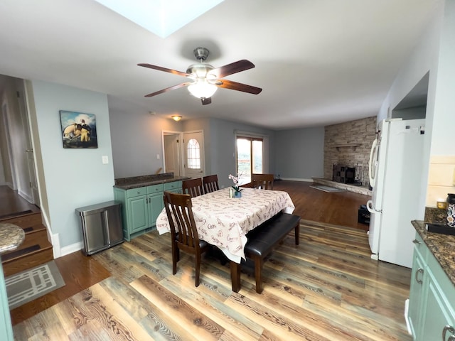 dining room with a skylight, a fireplace, ceiling fan, wood finished floors, and baseboards