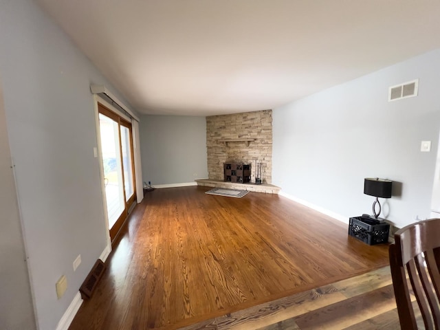 unfurnished living room with a stone fireplace, dark wood finished floors, visible vents, and baseboards