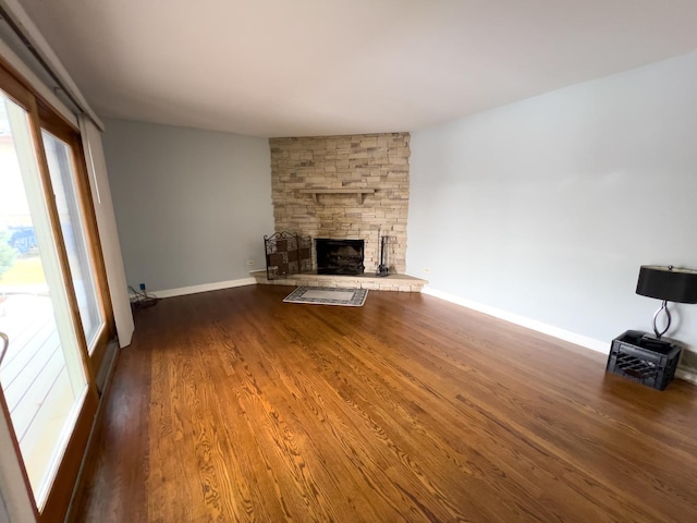 unfurnished living room featuring dark wood-style floors, a stone fireplace, and baseboards