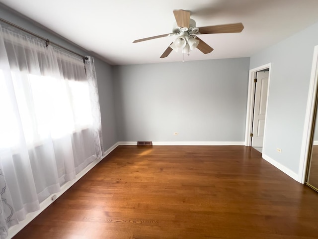 empty room featuring dark wood-type flooring, a ceiling fan, visible vents, and baseboards