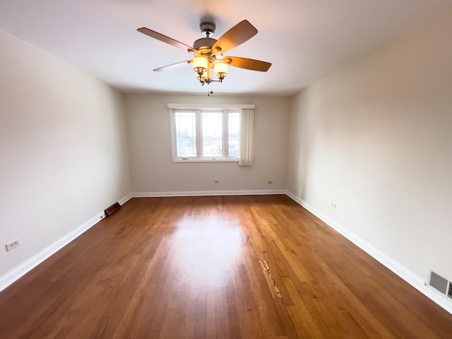 spare room with ceiling fan, visible vents, baseboards, and wood finished floors