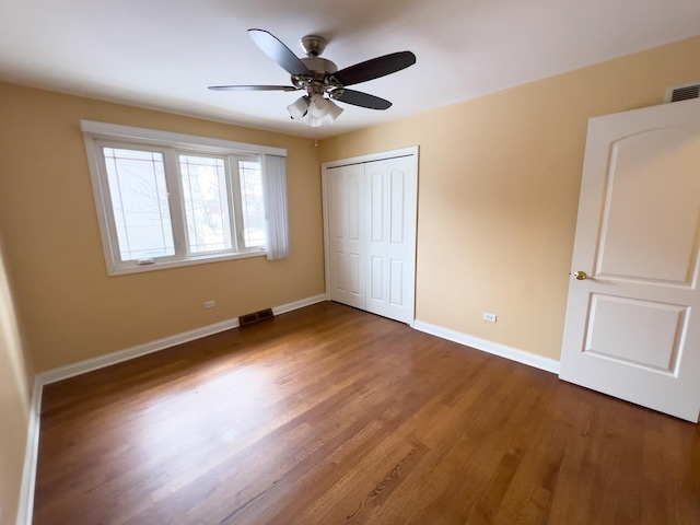 unfurnished bedroom with a closet, wood finished floors, visible vents, and baseboards