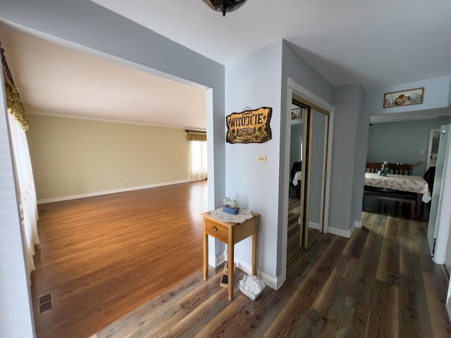 corridor featuring dark wood-style flooring, visible vents, and baseboards