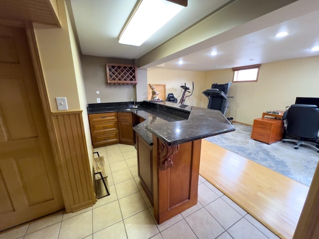 kitchen featuring brown cabinetry, open floor plan, a sink, and dark stone countertops