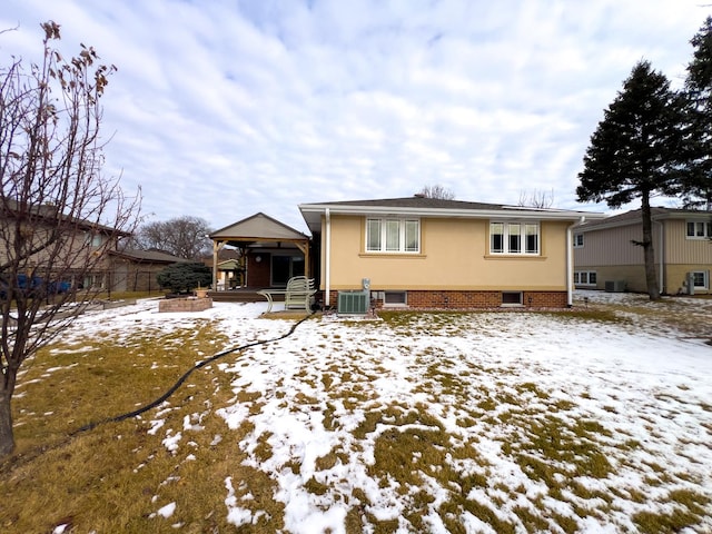 snow covered back of property featuring brick siding and central AC