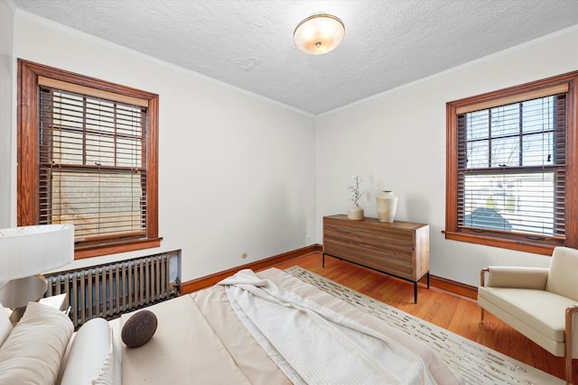 bedroom with crown molding, radiator heating unit, a textured ceiling, wood finished floors, and baseboards