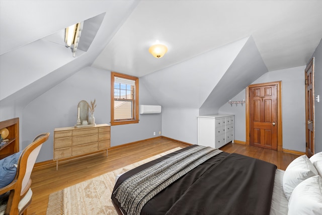 bedroom featuring a wall unit AC, vaulted ceiling, baseboards, and wood finished floors