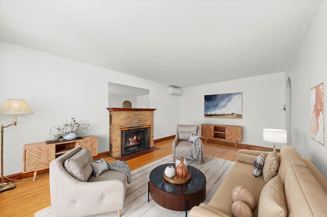 living room featuring arched walkways, a fireplace, a wall mounted AC, light wood-style floors, and baseboards