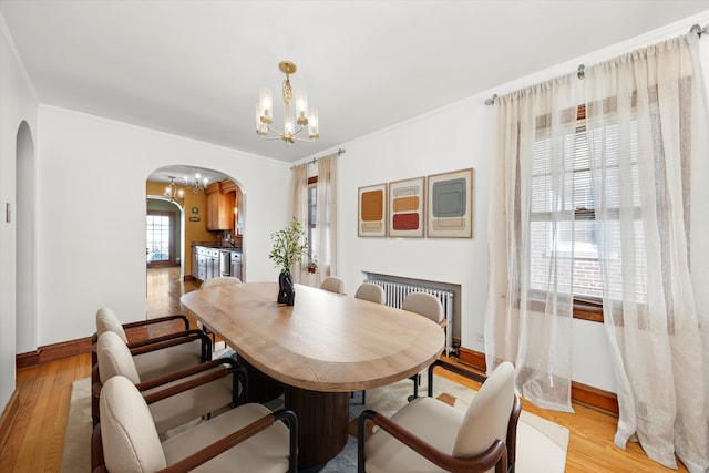 dining area featuring a chandelier, ornamental molding, arched walkways, and light wood-style floors