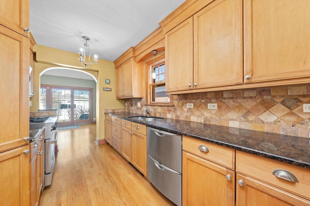 kitchen featuring arched walkways, stainless steel appliances, a sink, light wood finished floors, and tasteful backsplash