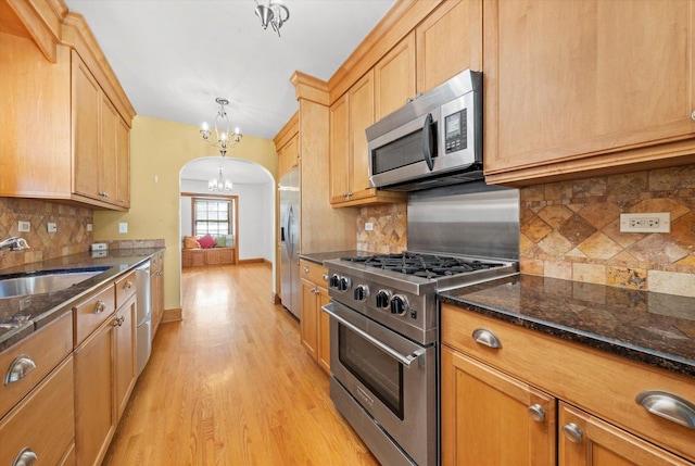 kitchen with arched walkways, a notable chandelier, a sink, appliances with stainless steel finishes, and light wood-type flooring