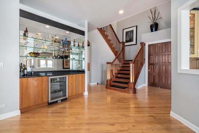 bar featuring light wood-type flooring, beverage cooler, wet bar, and stairs