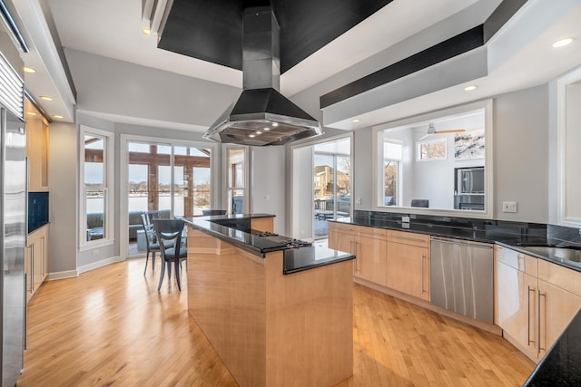 kitchen featuring light brown cabinets, island range hood, stainless steel dishwasher, and a breakfast bar area