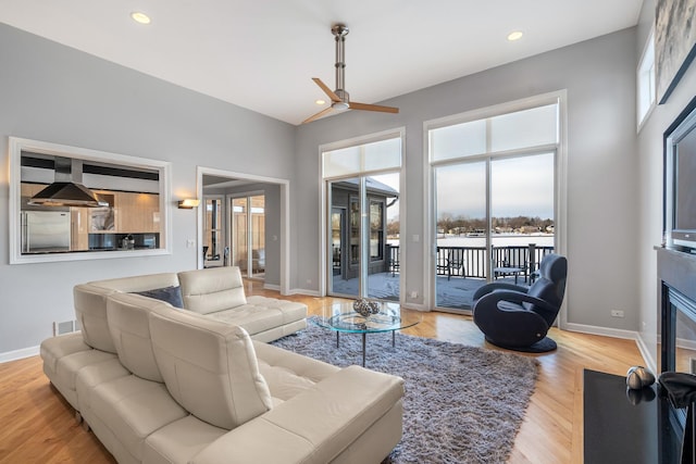 living room featuring a fireplace with flush hearth, light wood-type flooring, visible vents, and plenty of natural light