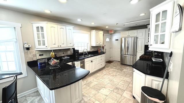 kitchen featuring stainless steel appliances, a peninsula, a sink, backsplash, and glass insert cabinets