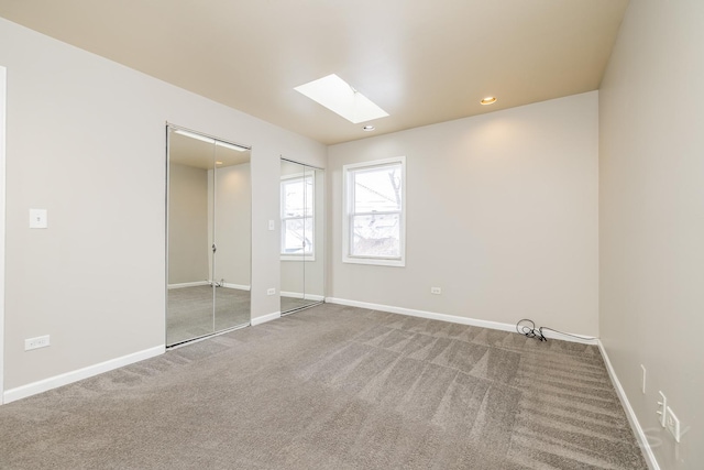 unfurnished bedroom with carpet floors, a skylight, two closets, recessed lighting, and baseboards