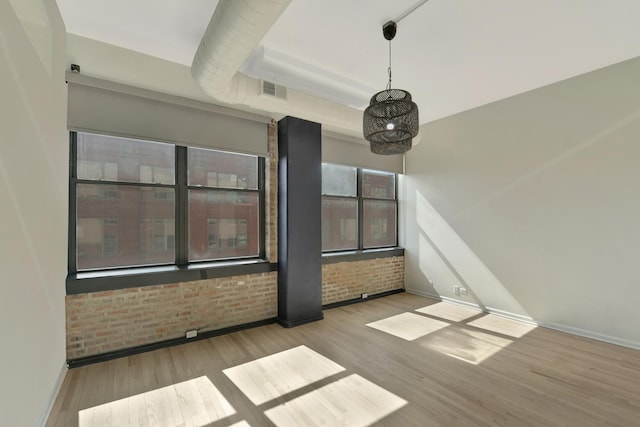 empty room with brick wall, light wood-style flooring, visible vents, and baseboards