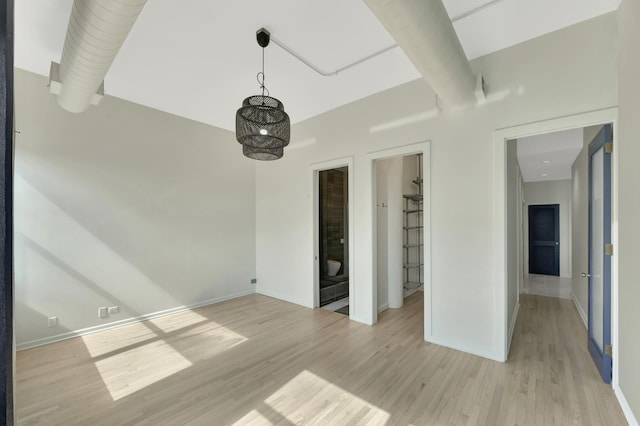 spare room with baseboards, beam ceiling, and light wood-style floors