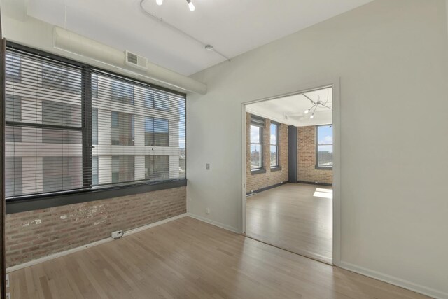 spare room with baseboards, visible vents, light wood finished floors, and brick wall