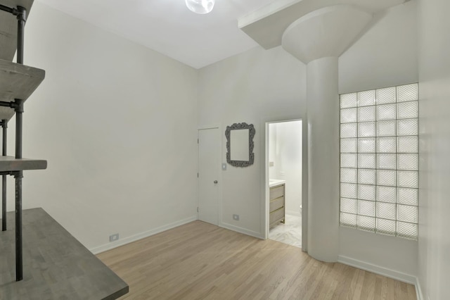 unfurnished bedroom featuring a high ceiling, baseboards, connected bathroom, and light wood finished floors