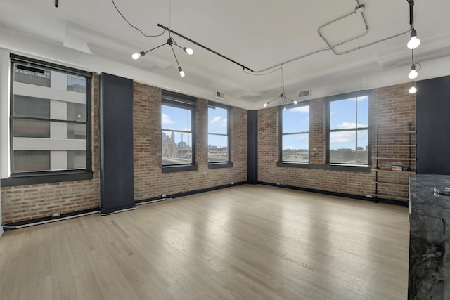 unfurnished room with visible vents, light wood-style flooring, and brick wall