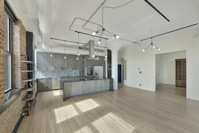 kitchen with stainless steel appliances, backsplash, island range hood, modern cabinets, and light wood-type flooring