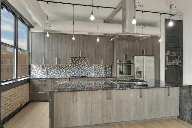 kitchen featuring modern cabinets, appliances with stainless steel finishes, dark stone counters, and decorative light fixtures