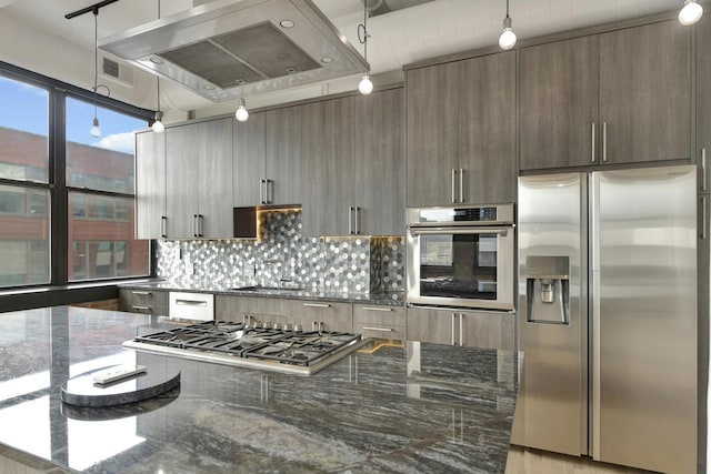 kitchen featuring dark stone counters, appliances with stainless steel finishes, island exhaust hood, and pendant lighting