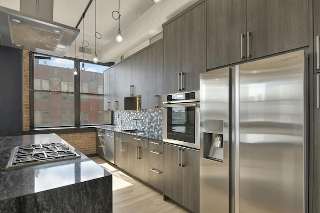 kitchen featuring hanging light fixtures, appliances with stainless steel finishes, dark stone countertops, and wall chimney range hood