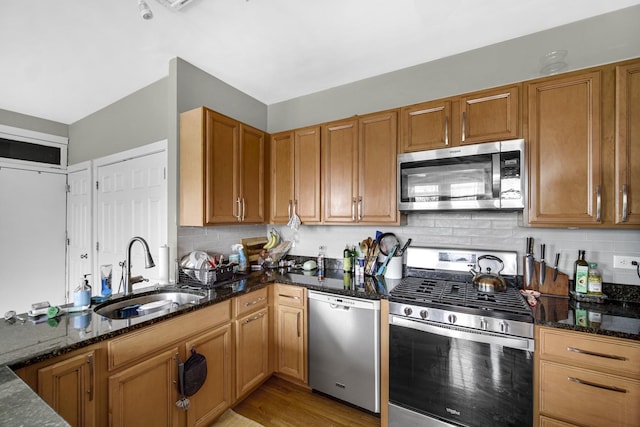 kitchen with dark stone counters, stainless steel appliances, a sink, and brown cabinets