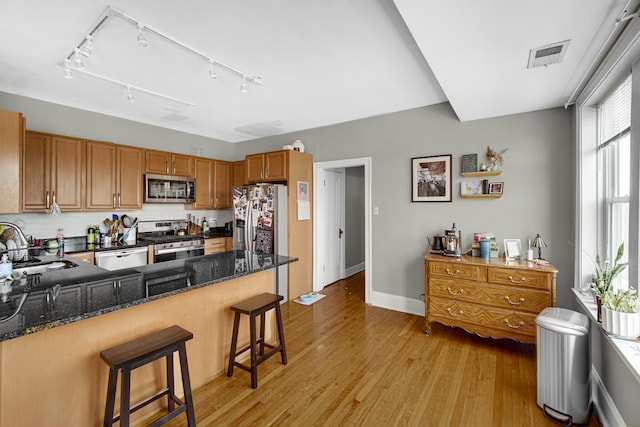 kitchen featuring light wood finished floors, visible vents, appliances with stainless steel finishes, a peninsula, and a kitchen bar