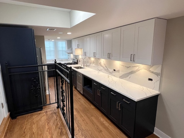 kitchen with white cabinetry, a sink, dark cabinets, stainless steel gas range, and wall chimney exhaust hood