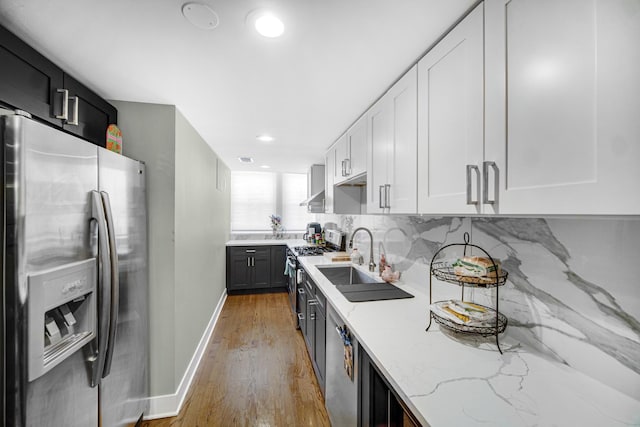 kitchen featuring white cabinets, appliances with stainless steel finishes, light stone counters, wall chimney range hood, and a sink